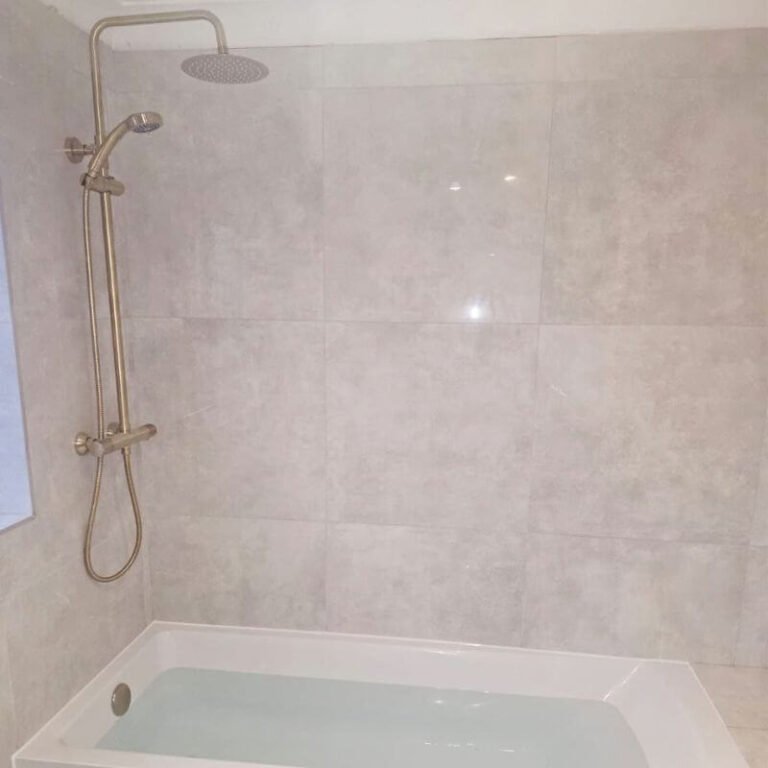 Bath with brushed brass thermostatic rain shower and large grey wall tiles